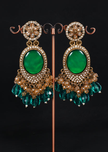 A pair of ornate gold-toned statement earrings with large oval green stones and dangling green crystal drops.