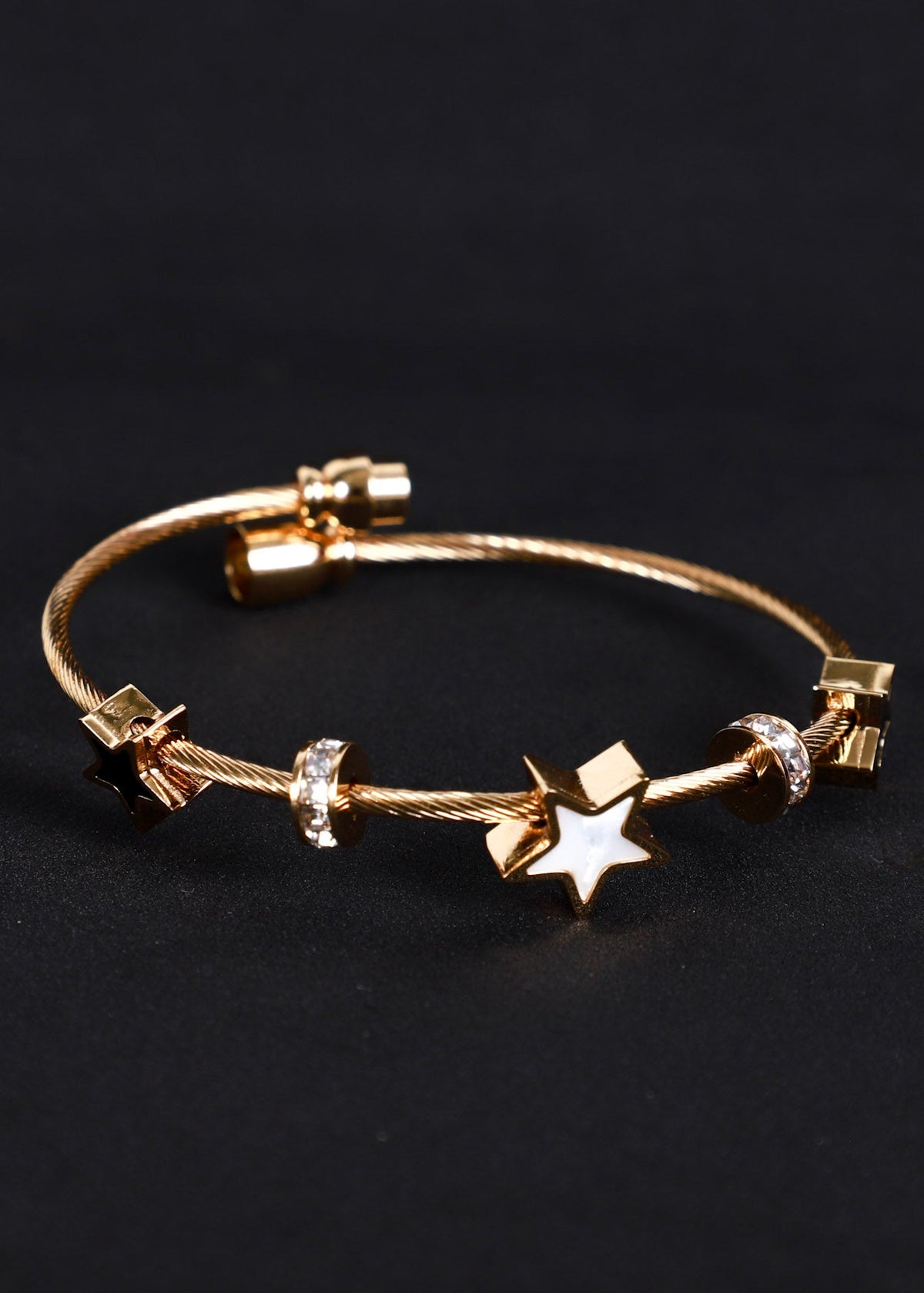 A gold-plated cable wire bracelet featuring multiple star and crescent moon charms, some adorned with small clear crystals, displayed on a dark black background.