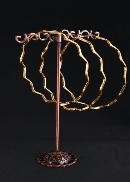 A decorative jewelry display stand with three wavy circular rings on a vertical stem, finished in a metallic copper/bronze tone against a black background.