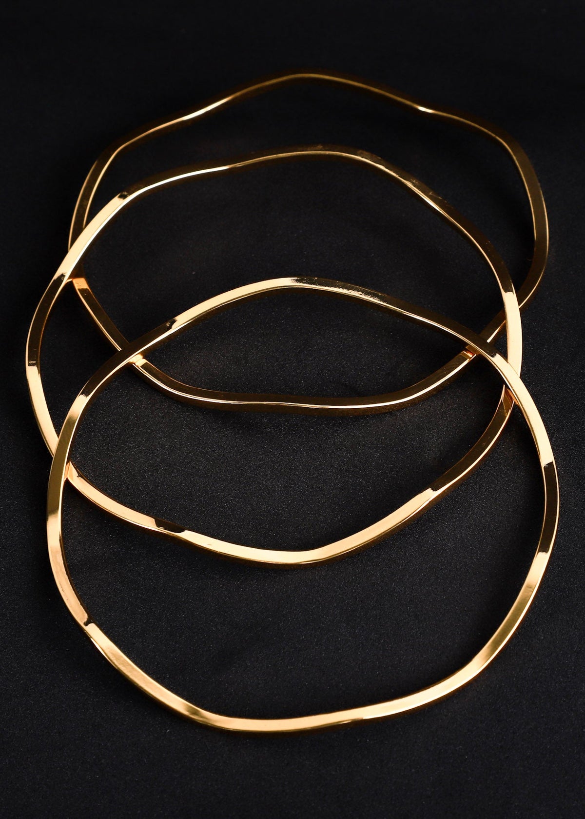 Three thin, polished gold-tone metal rings arranged in an overlapping stack on a dark black background.