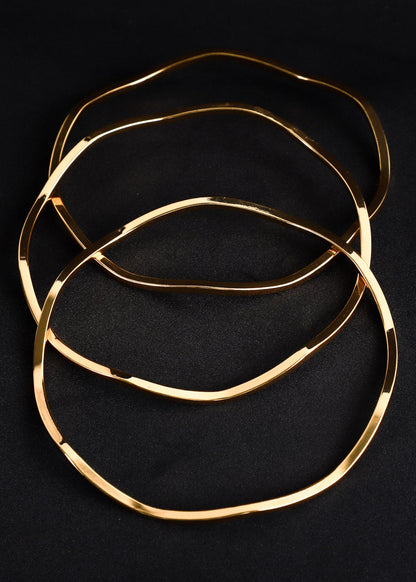 Three thin, polished gold-tone metal rings arranged in an overlapping stack on a dark black background.