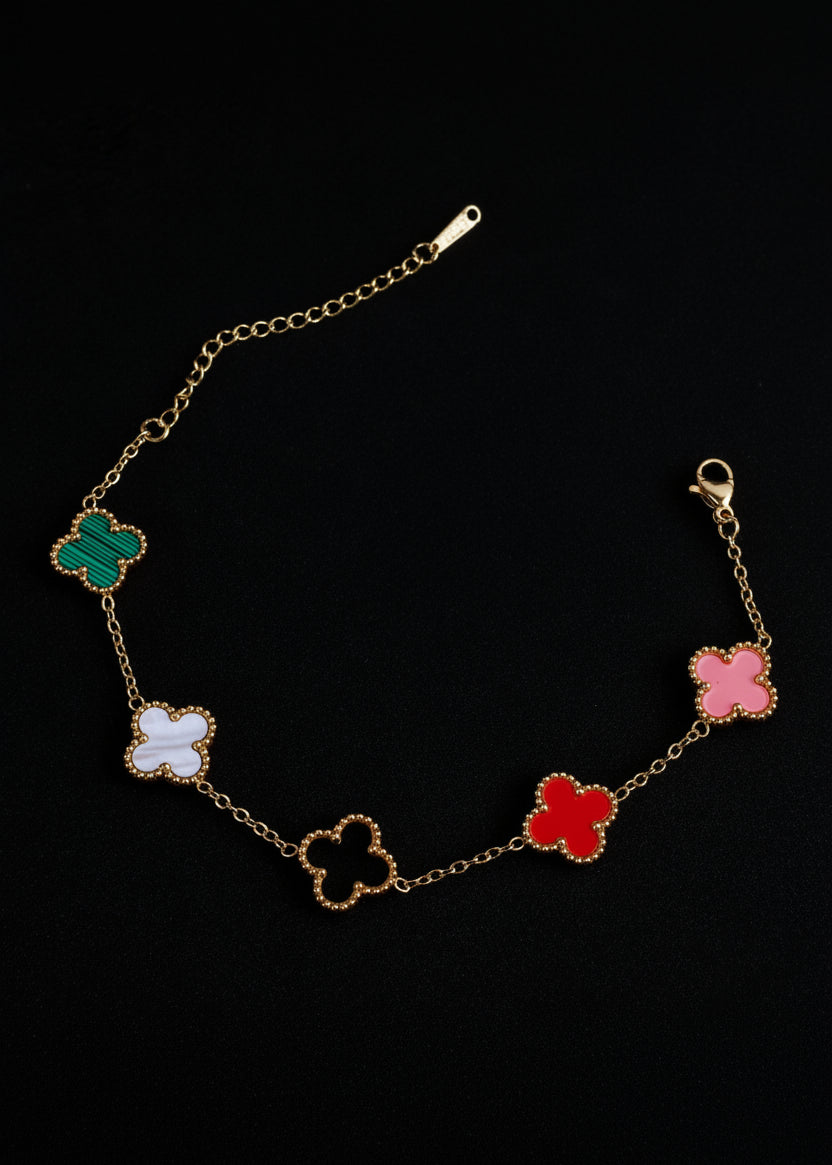 A gold chain bracelet featuring five colorful four-leaf clover motifs in green, white, beige, red, and pink, displayed on a black background.