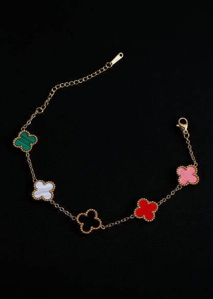 A gold chain bracelet featuring five colorful four-leaf clover motifs in green, white, beige, red, and pink, displayed on a black background.