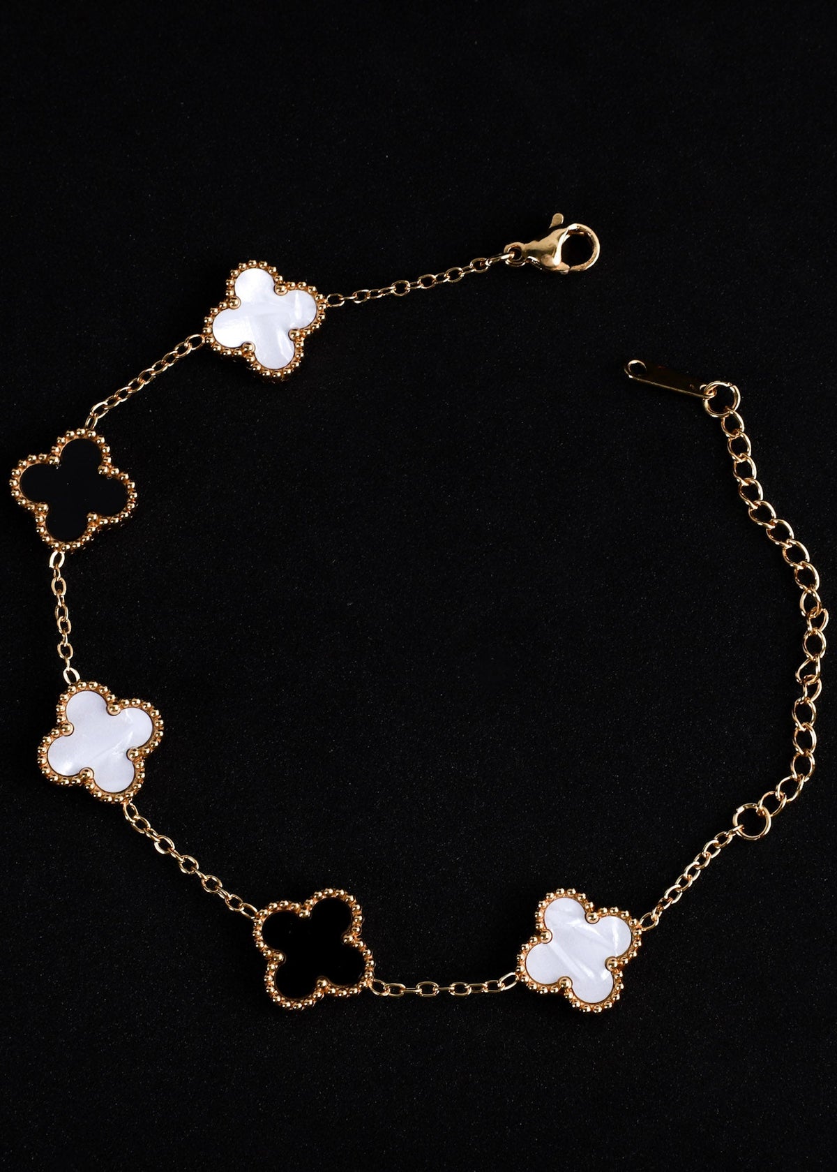 A gold chain bracelet featuring five clover-shaped links with white inlay, displayed on a solid black background.