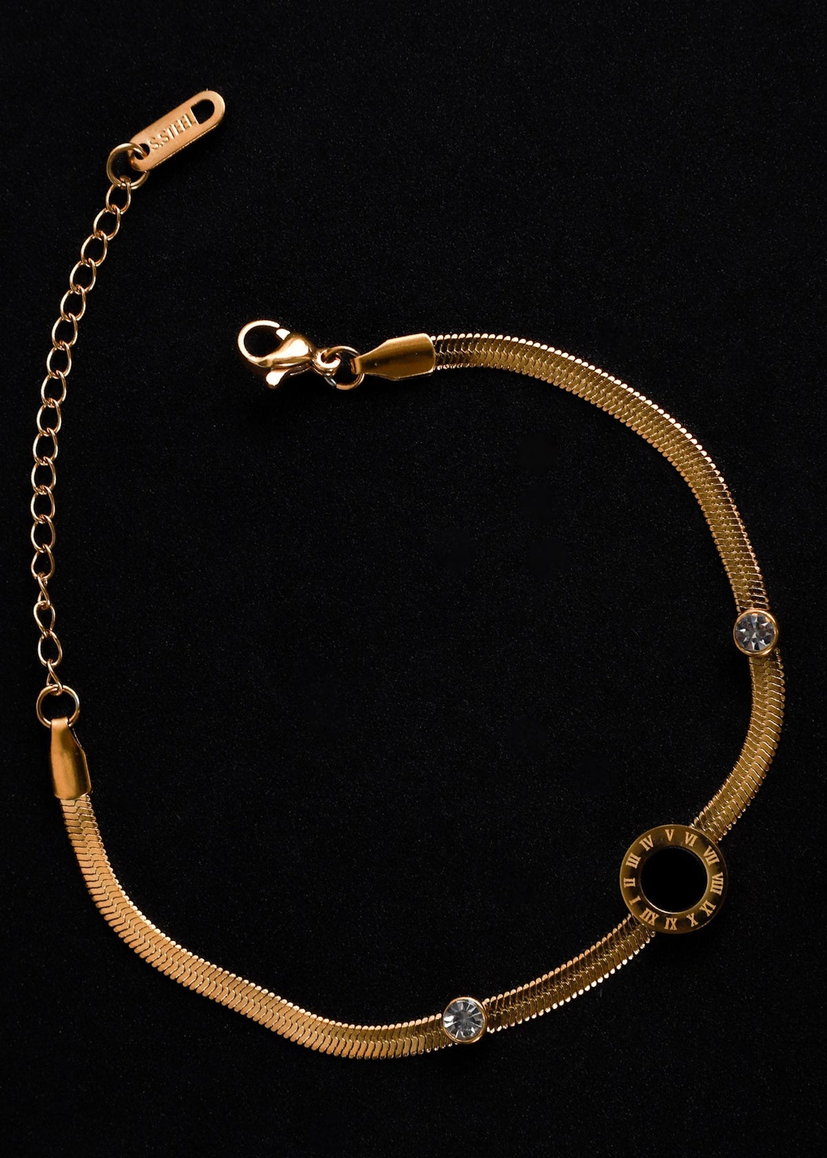 A gold-toned snake chain bracelet with a circular ring charm and two clear rhinestone accents, displayed on a black background.