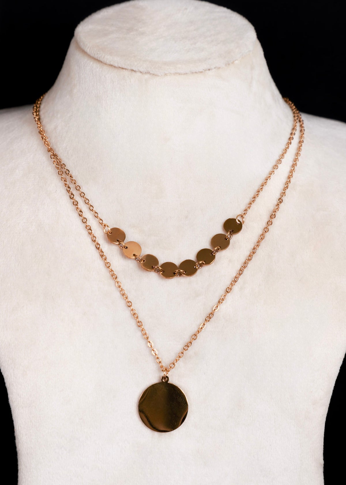 A double-strand anti tarnish gold-tone necklace displayed on a white fabric mannequin bust. The top layer features a row of small flat gold discs, while the longer bottom layer hangs down to a larger oval gold pendant.