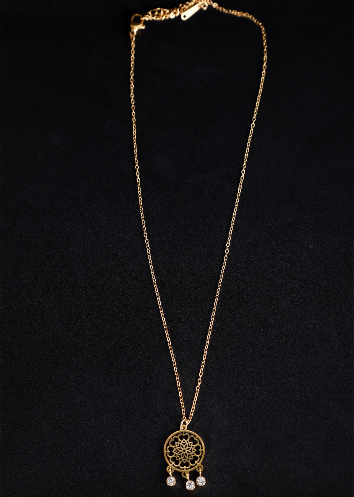 A gold-toned dreamcatcher necklace with a detailed web design pendant and small dangling clear beads, displayed against a solid black background.