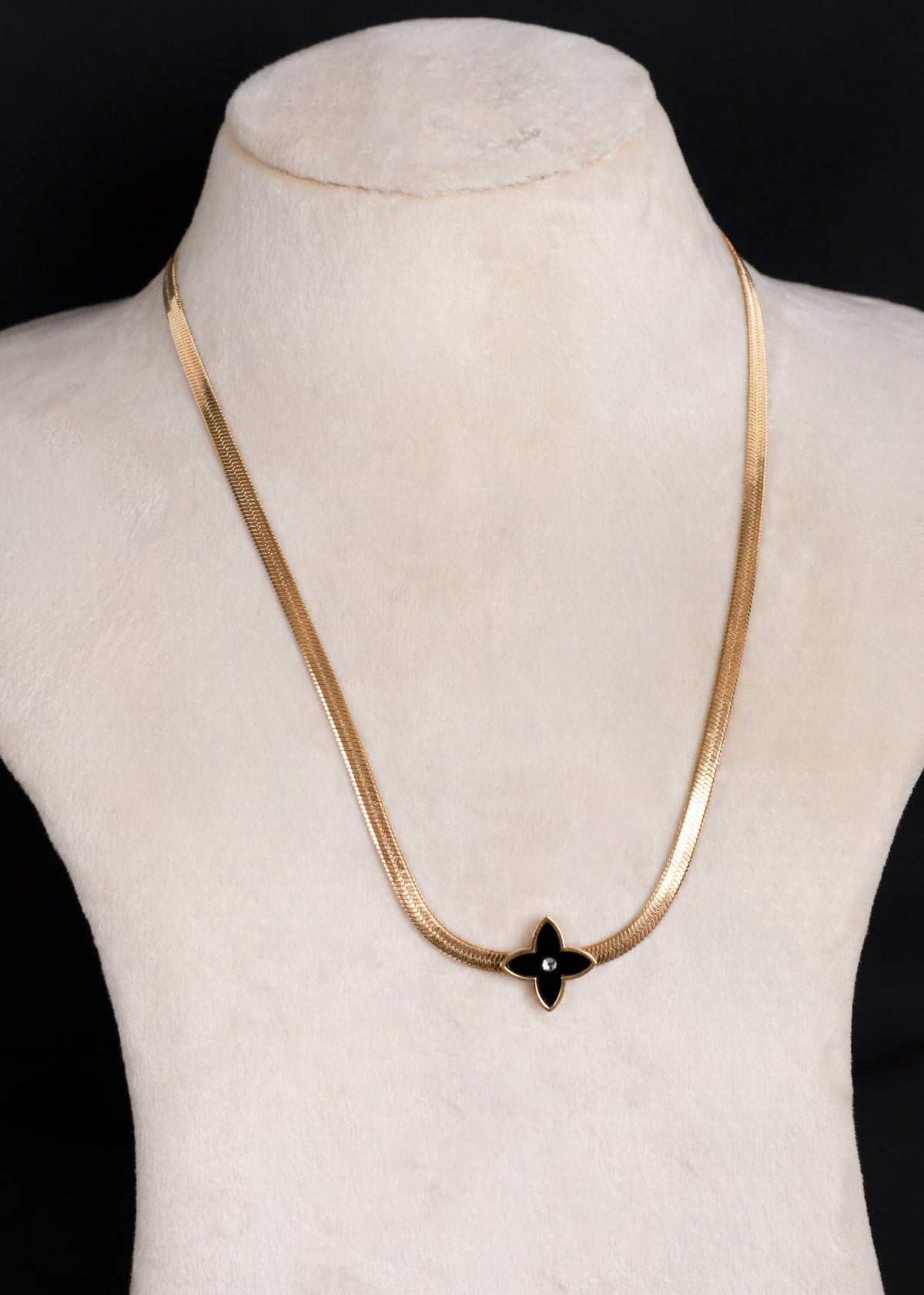 A gold-tone anti-tarnish snake chain necklace with a black onyx flower pendant, displayed on a cream-colored mannequin bust against a black background.