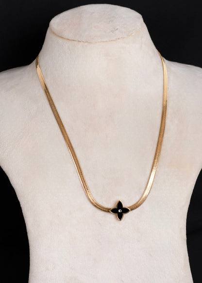 A gold-tone anti-tarnish snake chain necklace with a black onyx flower pendant, displayed on a cream-colored mannequin bust against a black background.