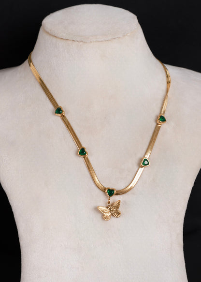 Anti tarnish gold-tone snake chain necklace displayed on a cream-colored mannequin bust. The necklace features five small green heart-shaped stones spaced along the chain, with a gold butterfly pendant hanging from a green heart at the center.