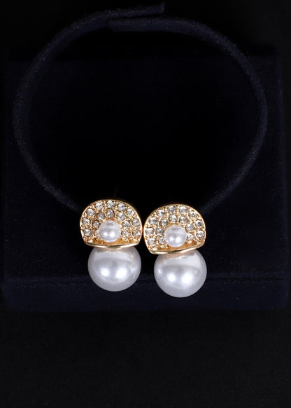 A pair of gold and pearl stud earrings displayed on a black velvet jewelry stand against a black background.