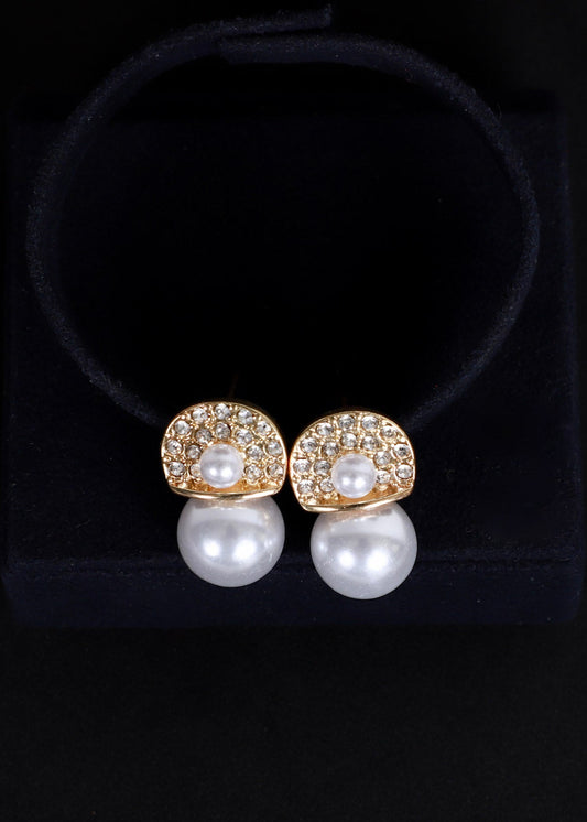 A pair of gold and pearl stud earrings displayed on a black velvet jewelry stand against a black background.