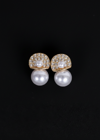A pair of gold and pearl stud earrings with pavé-set clear stones, shown on a solid black background.