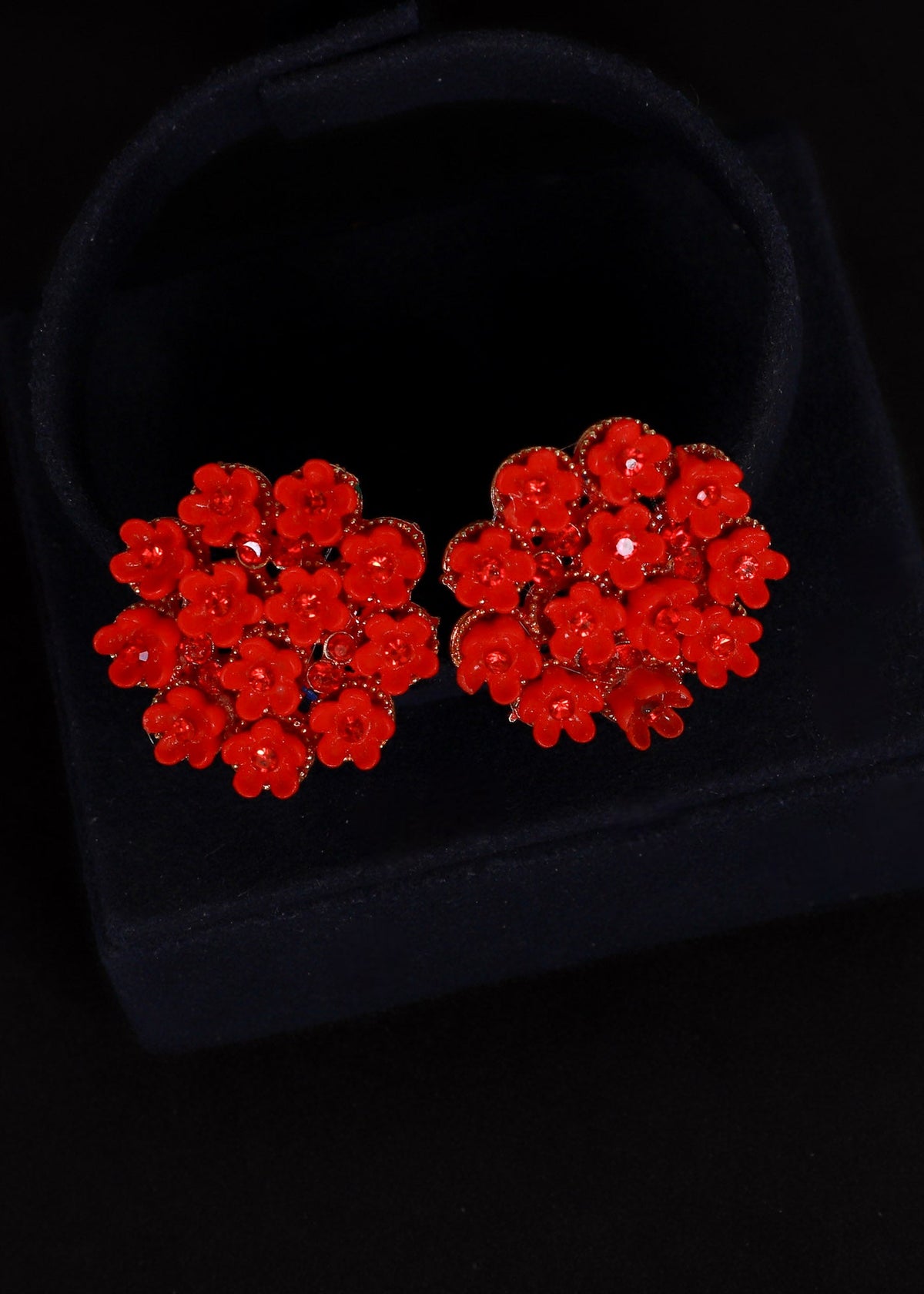 A pair of red floral stud earrings displayed on a black velvet jewelry box against a black background.