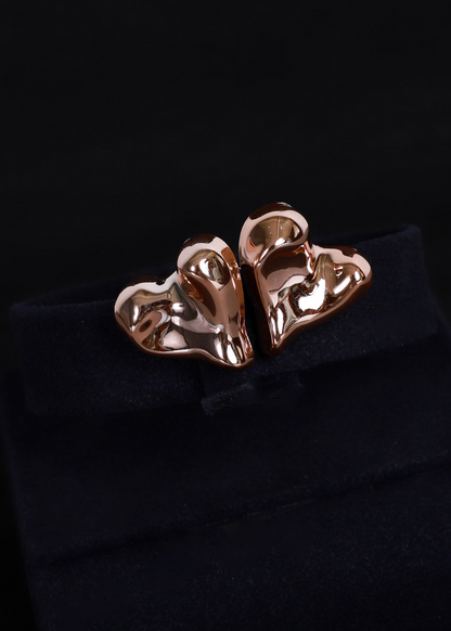 A pair of rose gold abstract sculptural stud earrings displayed on a black velvet jewelry box against a black background.