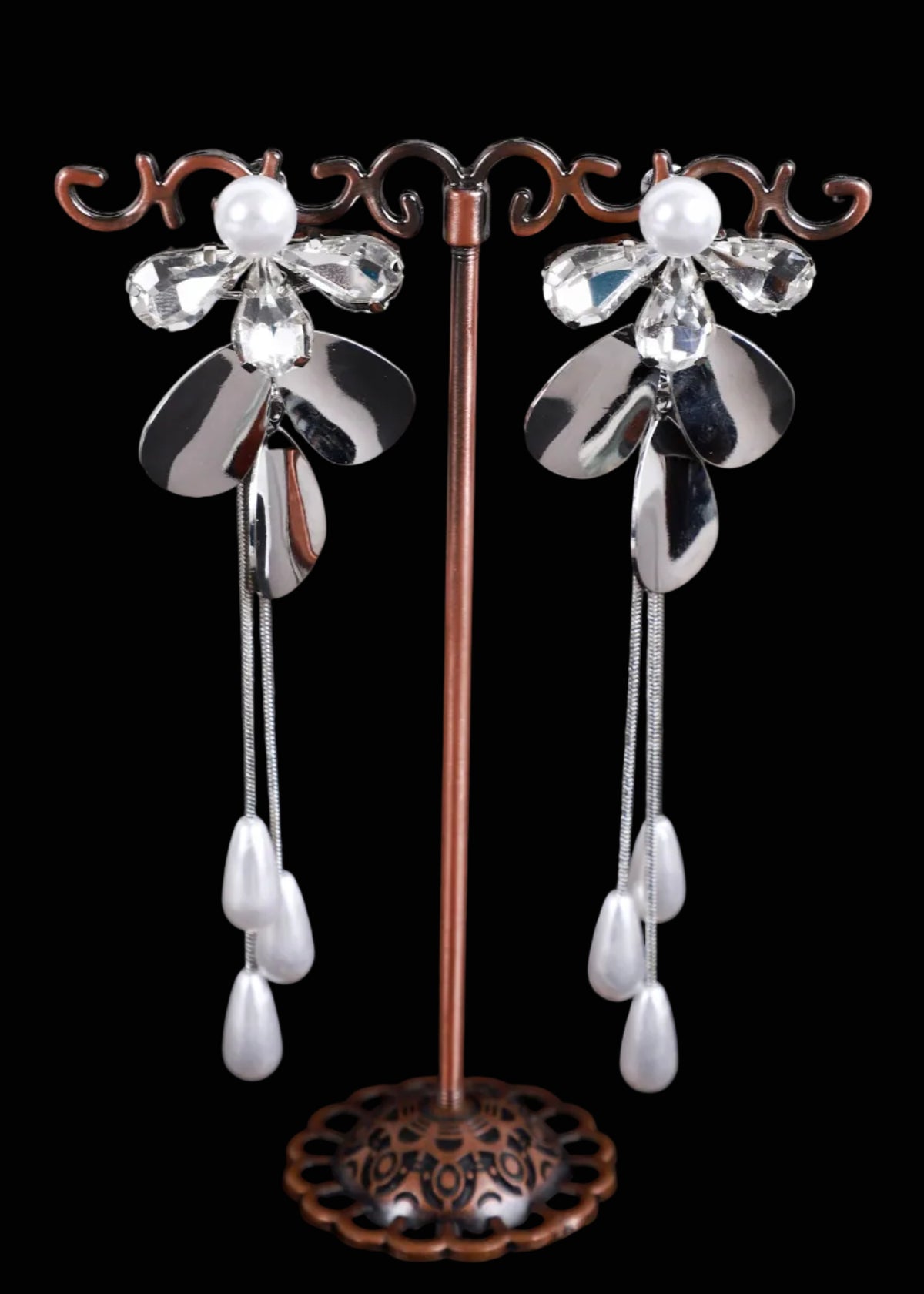 A pair of dangling flower-shaped earrings. Each earring has a silver-toned flower with clear faceted crystal petals, a white pearl-like center, and two long silver chains ending in white teardrop beads.