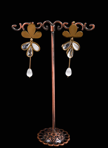 A pair of dangling earrings. The earrings feature a gold-tone floral top with clear teardrop-shaped crystals and a white teardrop drop.