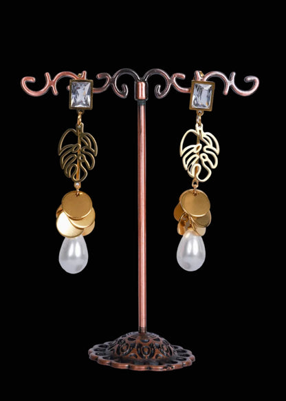 A pair of dangling earrings. Each earring has a clear rectangular gemstone, a gold-toned leaf-shaped charm, stacked gold coin charms, and a dangling clear teardrop pearl.