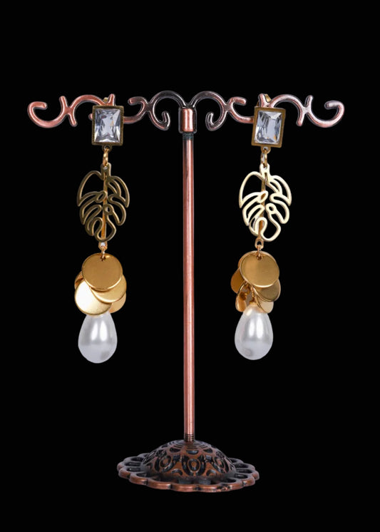 A pair of dangling earrings. Each earring has a clear rectangular gemstone, a gold-toned leaf-shaped charm, stacked gold coin charms, and a dangling clear teardrop pearl.