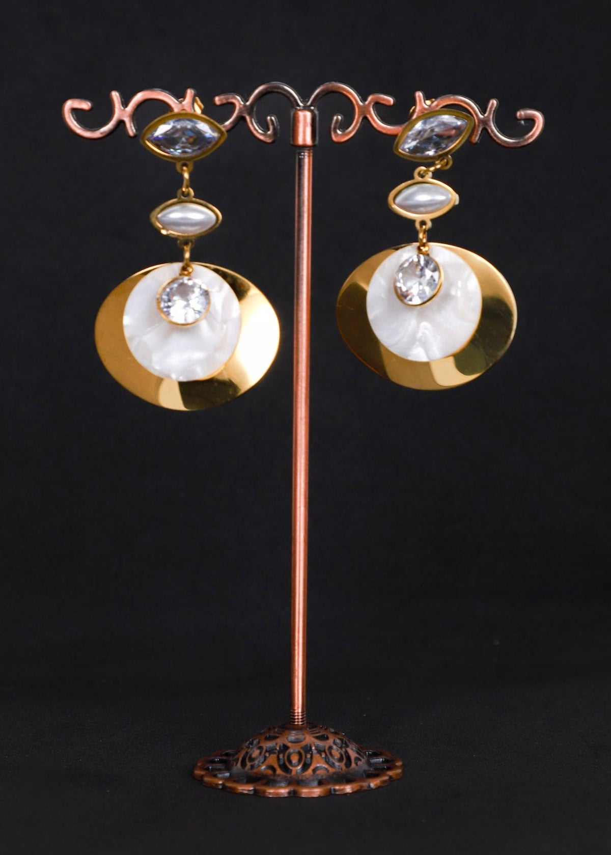 A pair of statement earrings. Each earring features a large round white mother-of-pearl disc with a gold-toned rim, a smaller oval white stone, a clear faceted center stone, and a small clear oval stone above.
